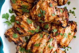 Yogurt Marinated Grilled Chicken shown from above on a white oval platter on a wooden table with a turquoise cloth to the side.