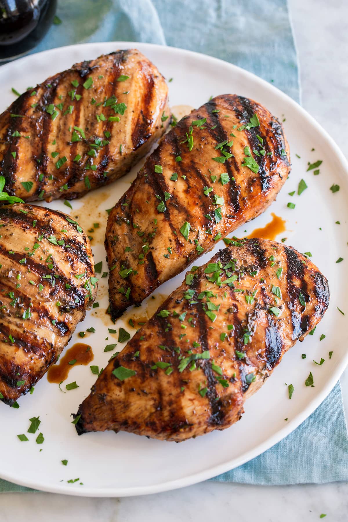 Balsamic Chicken Balsamic chicken breasts shown on a white plate over a blue cloth on a marble surface.