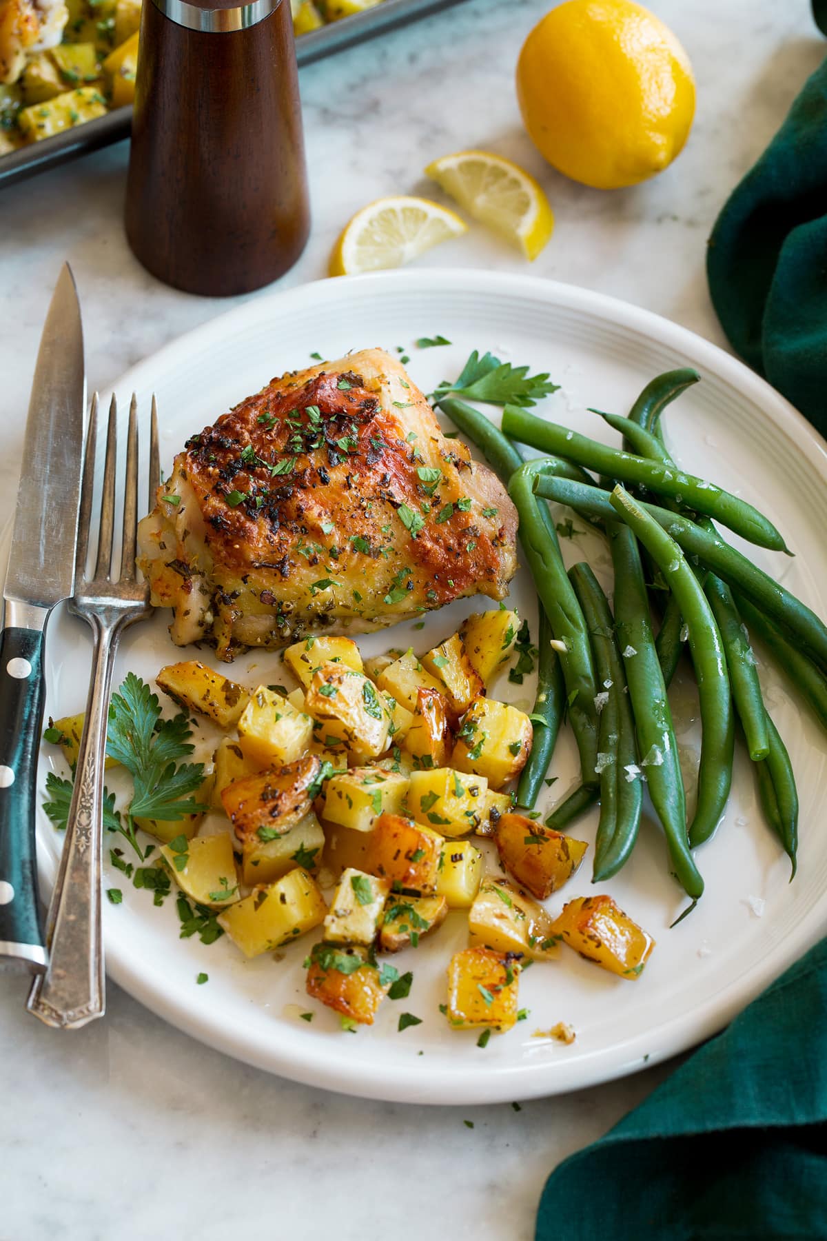 Baked Lemon Chicken and Potatoes Serving of chicken and potatoes on a white dinner plate shown with a side of steamed green beans as a serving suggestion.