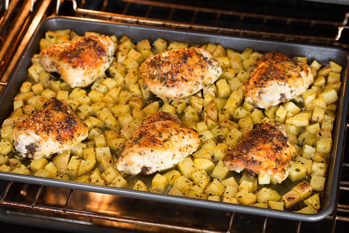 Baked Lemon Chicken and Potatoes Chicken and potatoes baking in the oven on a baking sheet.