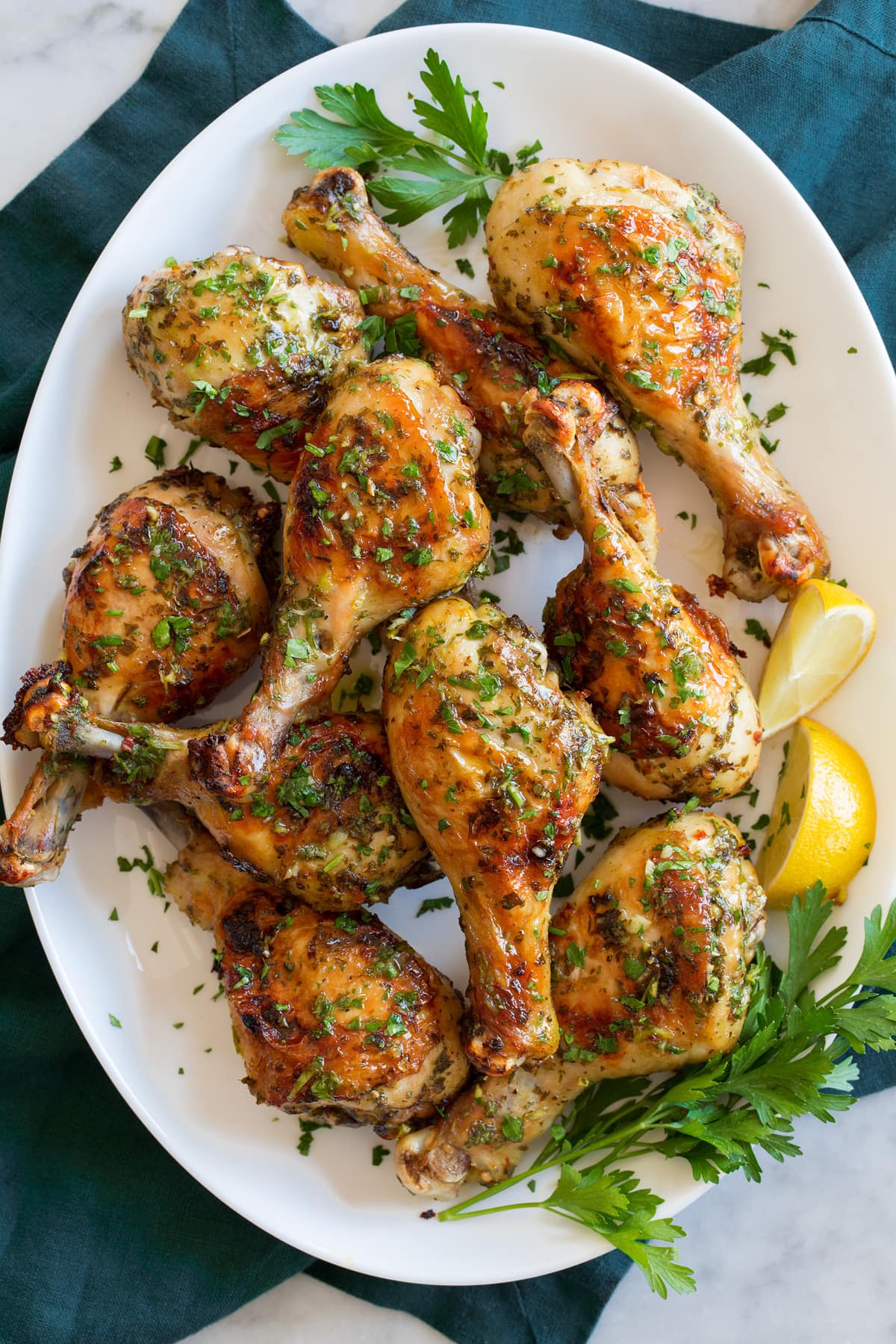 Baked Chicken Legs Baked chicken legs on a white oval platter with parsley and lemon wedges to the side.