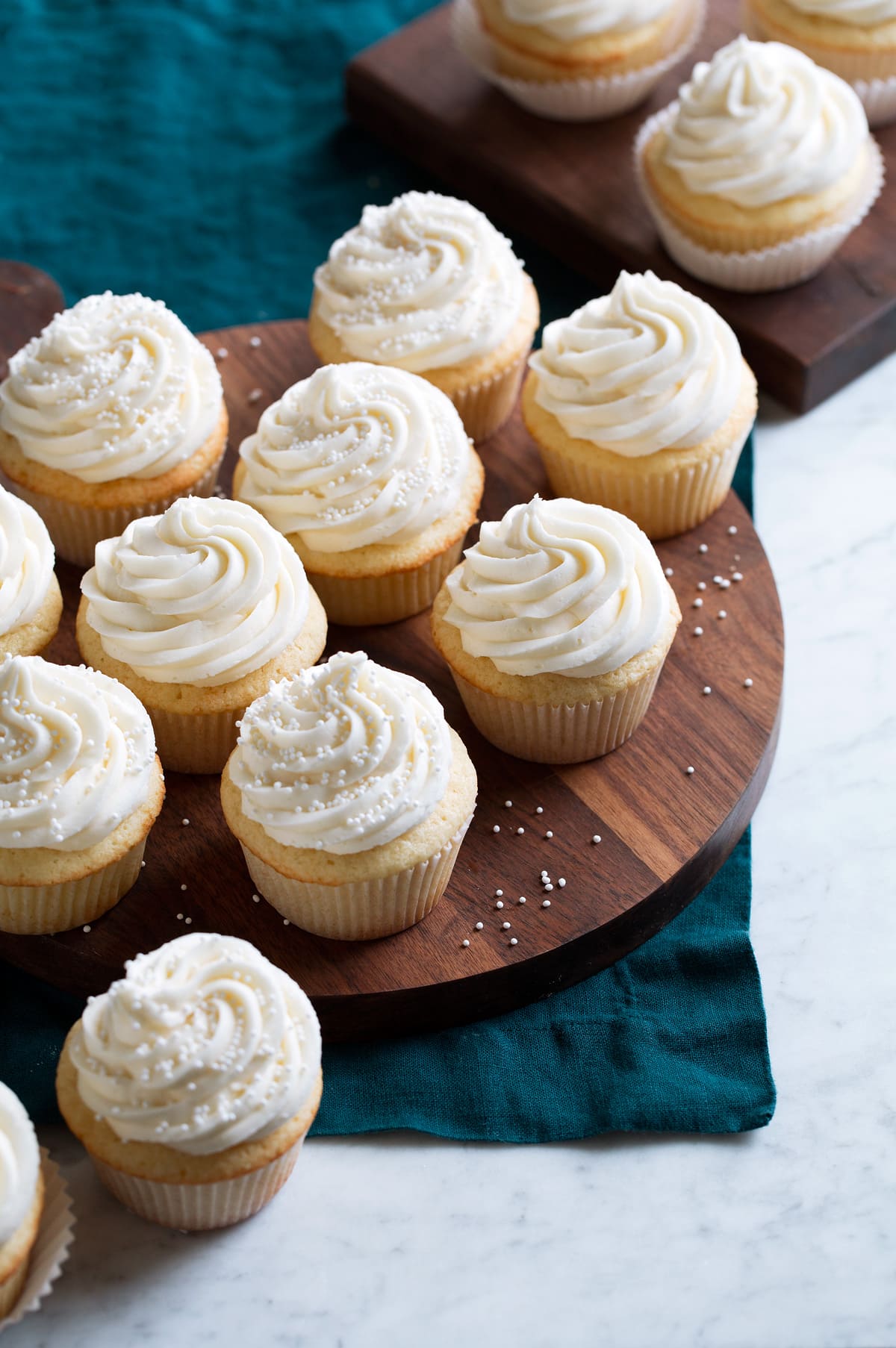 Vanilla Cupcakes A batch of homemade vanilla cupcakes shown on a wooden serving platter over a blue cloth.