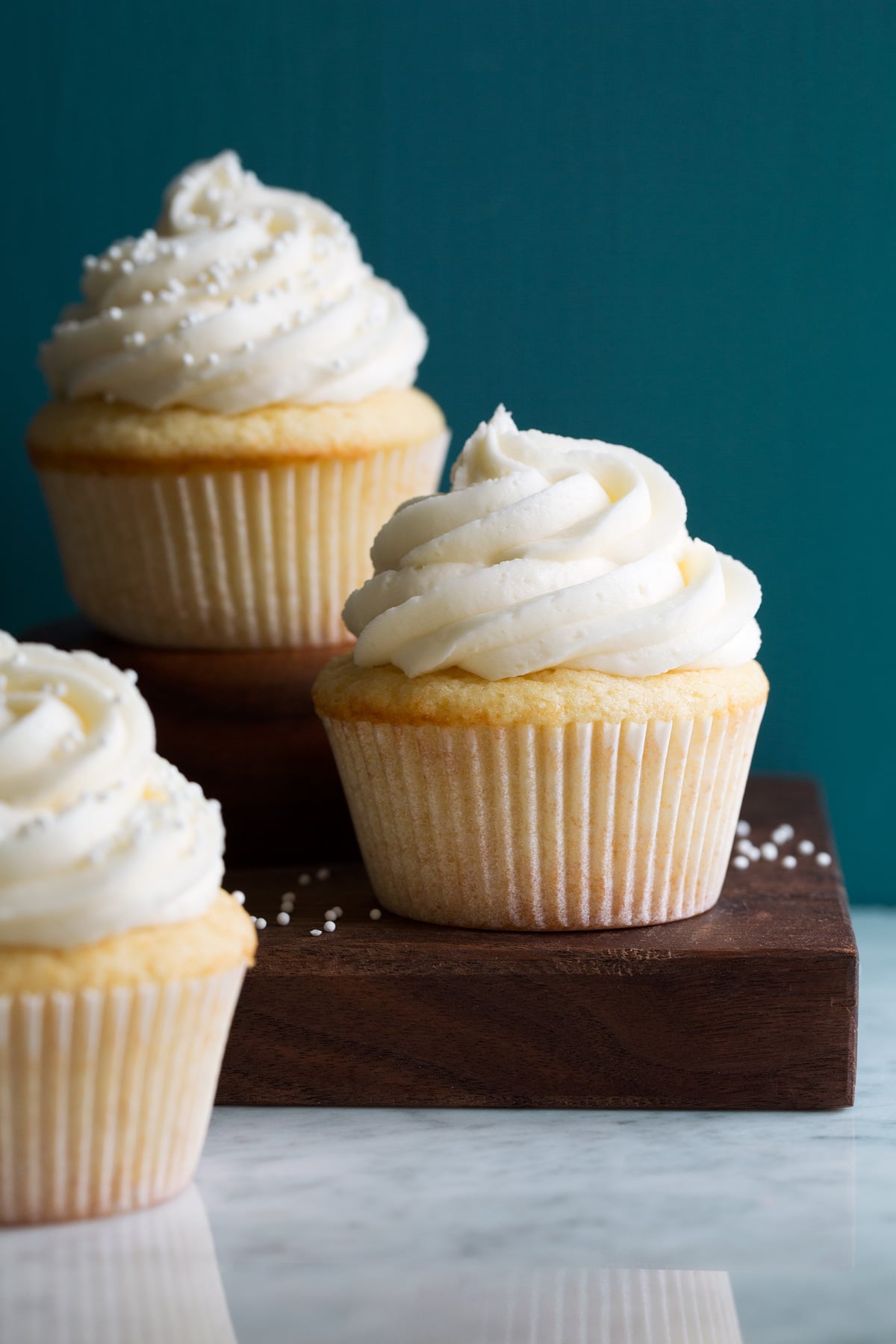 Photo of three vanilla cupcakes with vanilla buttercream frosting.