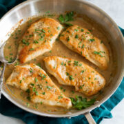 Chicken breasts in white wine and onion sauce in a skillet.