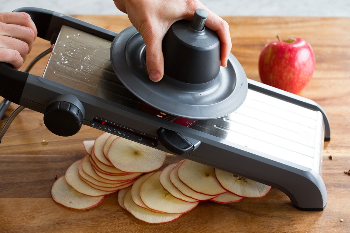 Baked Apple Chips Apples being sliced with a mandoline into thin slices over a wooden cutting board.