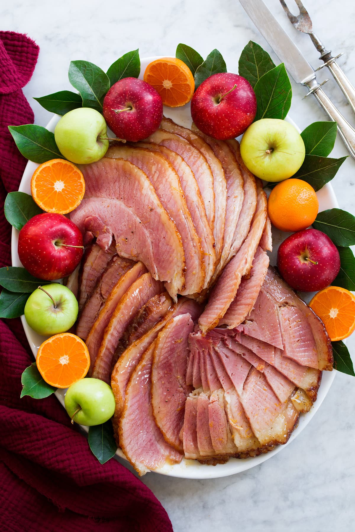 Crockpot Ham Sliced ham on a platter with fresh fruits and bay leaves.