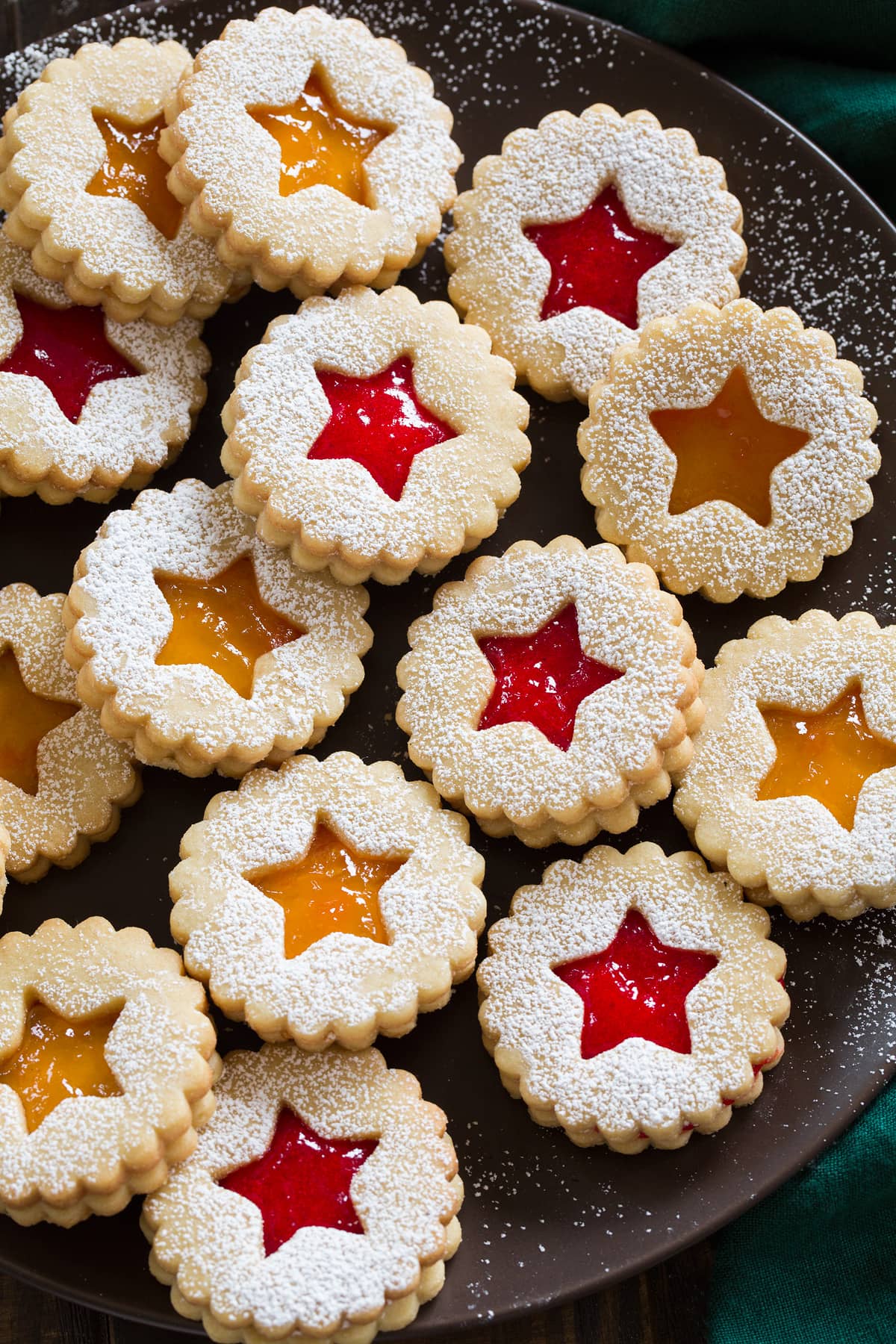 Linzer Cookies Powdered sugar dusted linzer cookies filled with fruit jam shown on a dark brown plate.