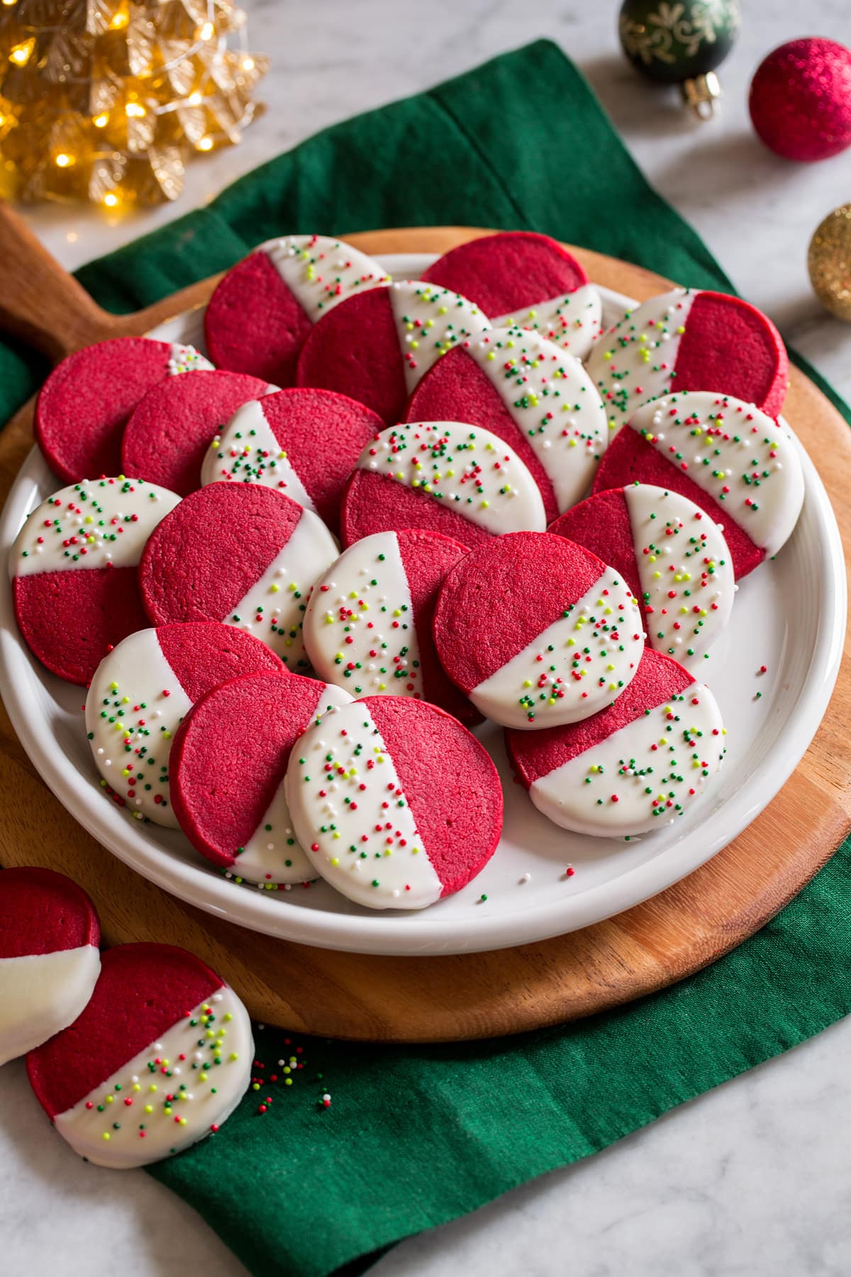 Red Velvet Shortbread Cookies Red velvet shortbread Christmas cookies shown piled on a white serving plate over a wooden platter and a rich green cloth.