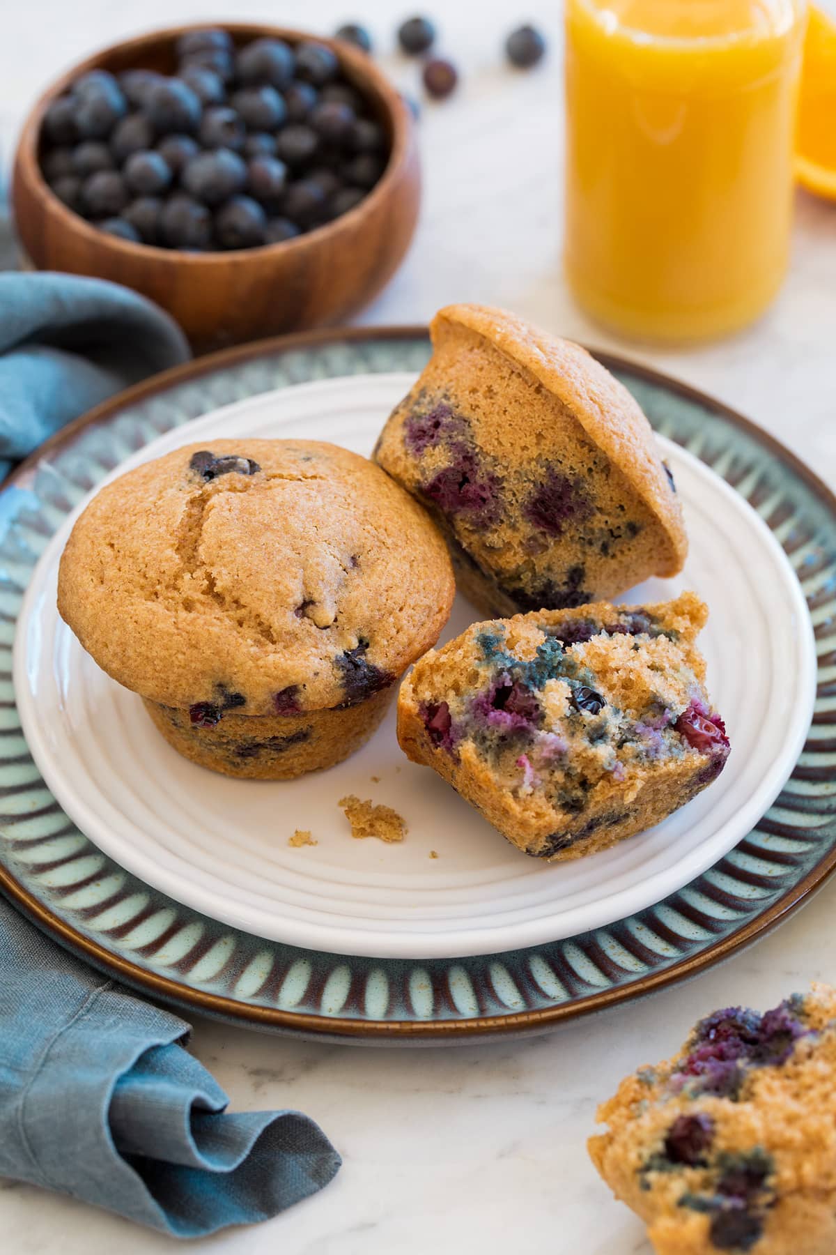 Healthy blueberry muffins on a white and blue plate with orange juice in the background.