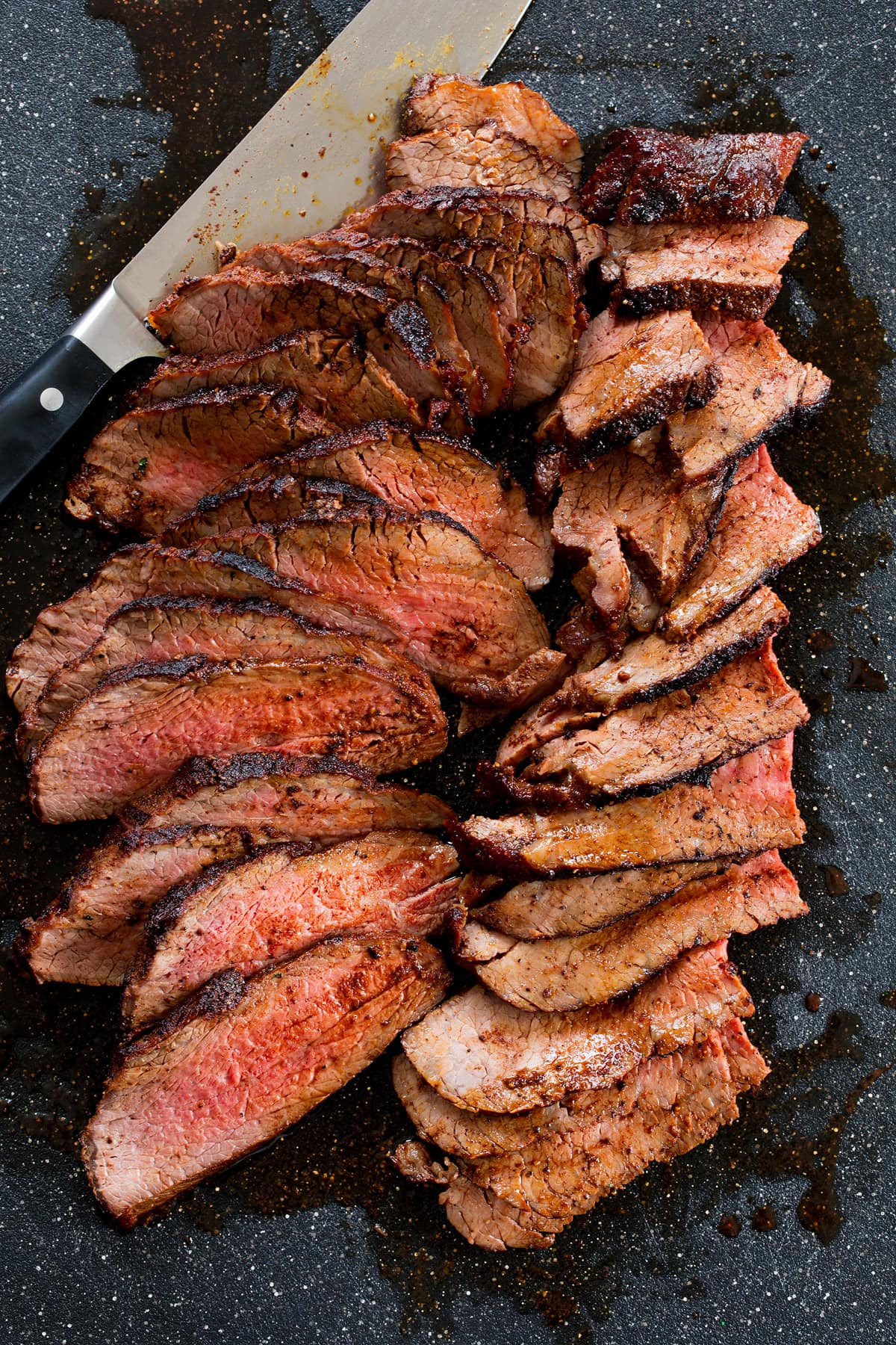 Roasted Tri Tip Overhead photo of tri tip being cut on a black cutting board with a chefs knife to the side.