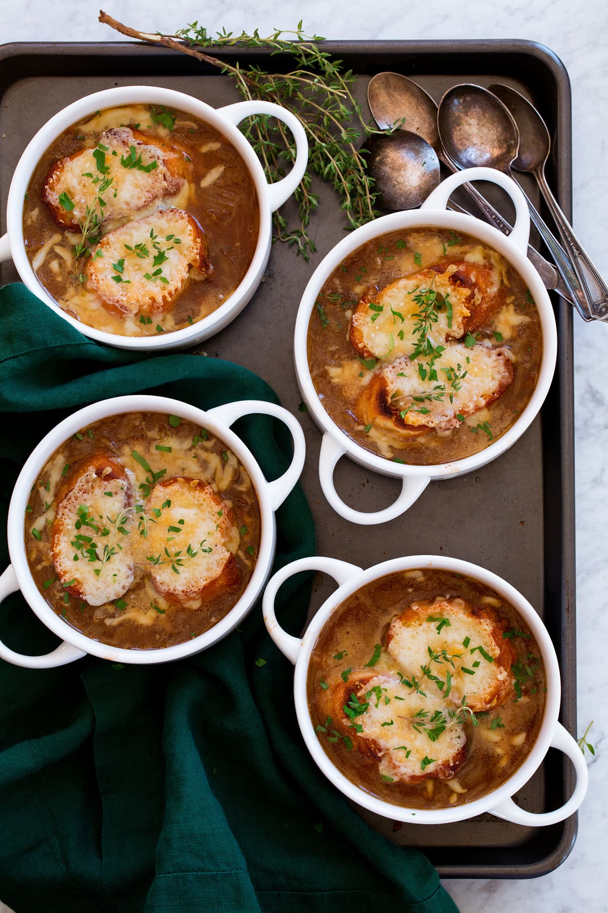 French Onion Soup Four servings of french onion soup in white bowls with handles, shown from overhead on a dark baking sheet.
