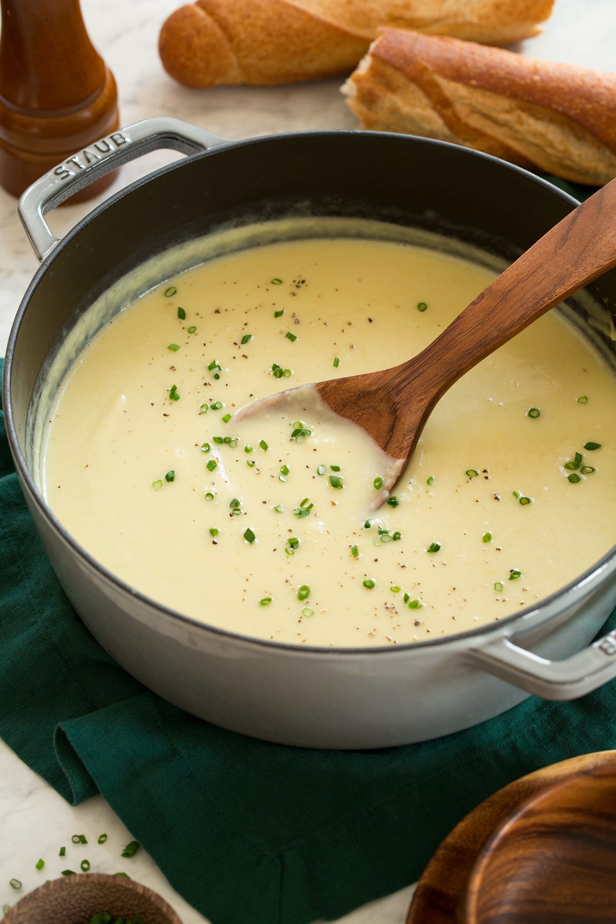 Potato Leek Soup Pot with potato leek soup garnished with chives and a wooden ladle is scooping soup.
