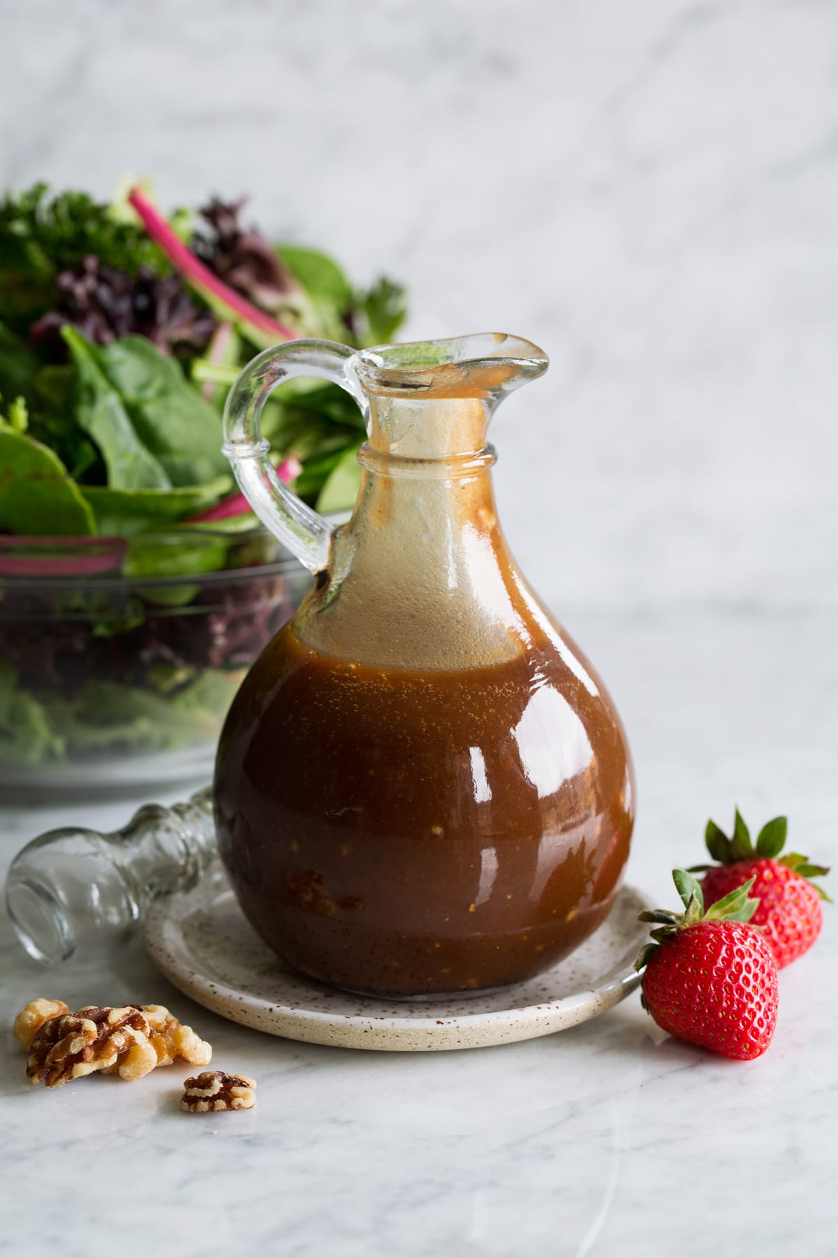Balsamic Vinaigrette Balsamic vinaigrette in a glass salad dressing jar set over a small plate. A green salad is shown in the background.