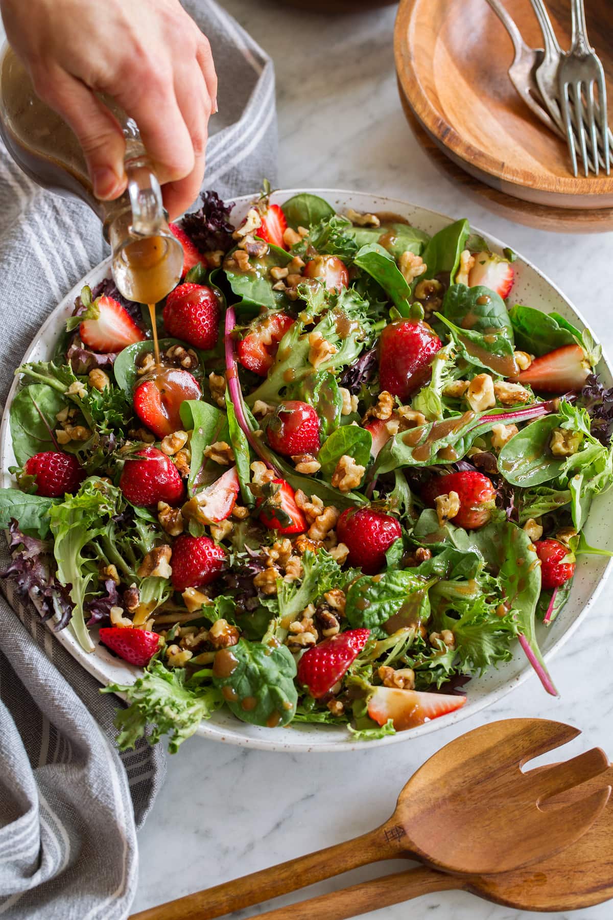 Balsamic Vinaigrette Green salad with strawberries and walnuts with balsamic vinaigrette being poured over.