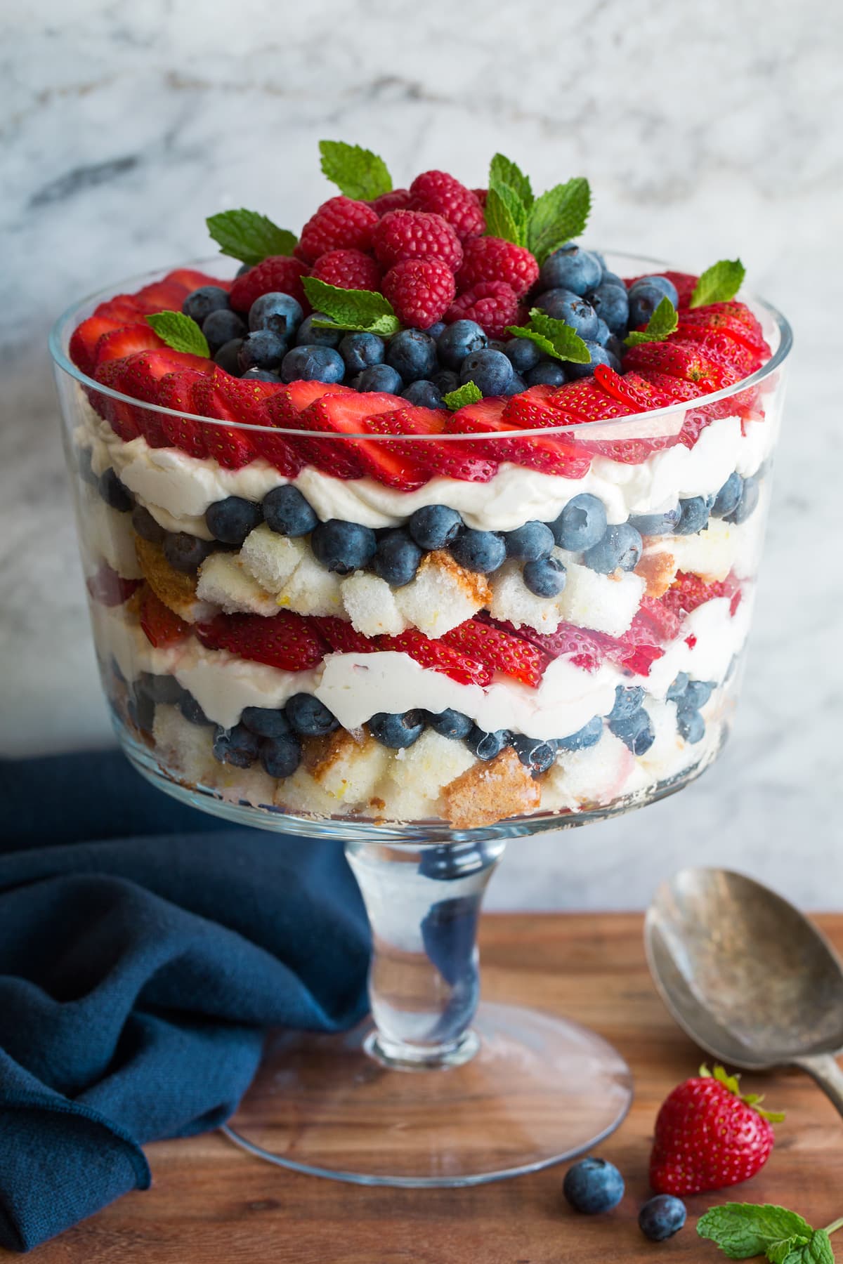 Trifle Layered trifle in a glass trifle dish. It includes cubes of angel food cake, blueberries, strawberries, raspberries and a cream cheese whipped cream topping.