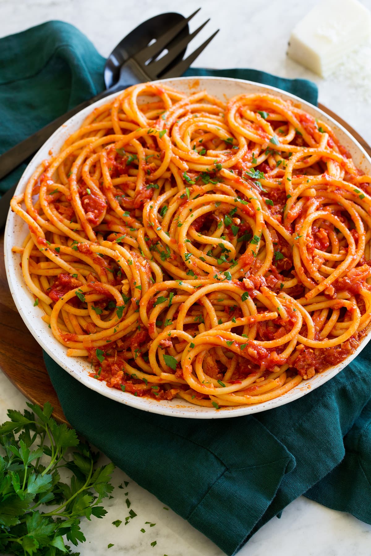 Bucatini all'Amatriciana Bucatini with amatriciana sauce in a white serving bowl with parmesan cheese and parsley garnish.