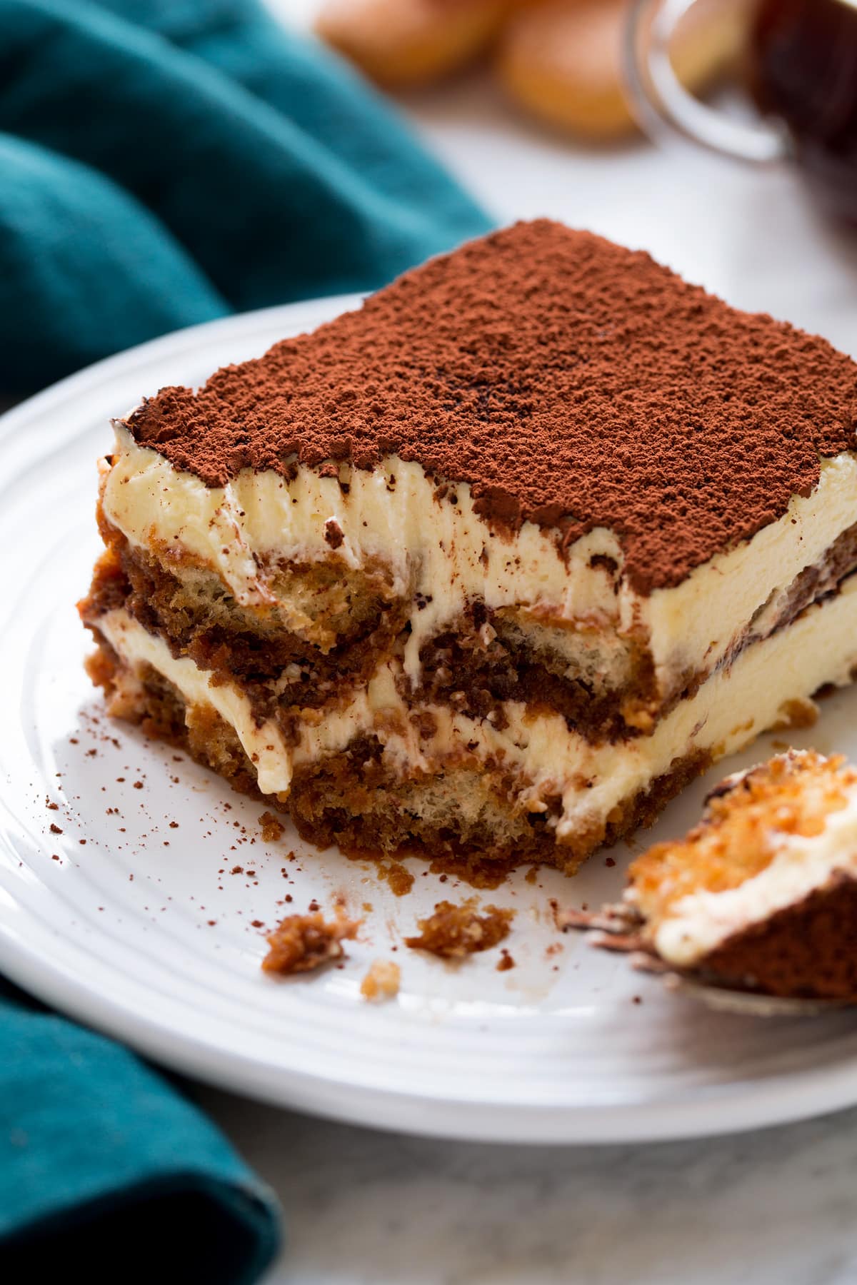 Tiramisu Close up photo of tiramisu cut into with a fork showing layers of custard filling, coffee soaked lady fingers and cocoa powder finish.