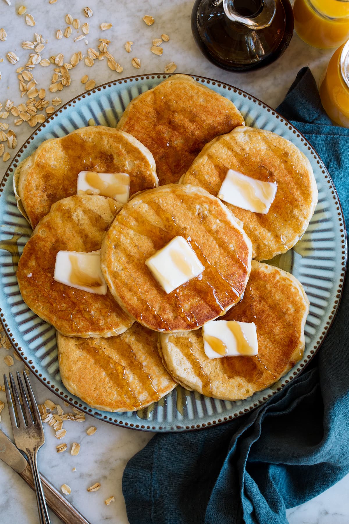 Oat Flour Pancakes Pancakes shown from overhead. They are spread out on a blue plate, topped with maple syrup drizzle and dabs of butter.