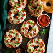Bagel pizzas on a dark baking sheet.