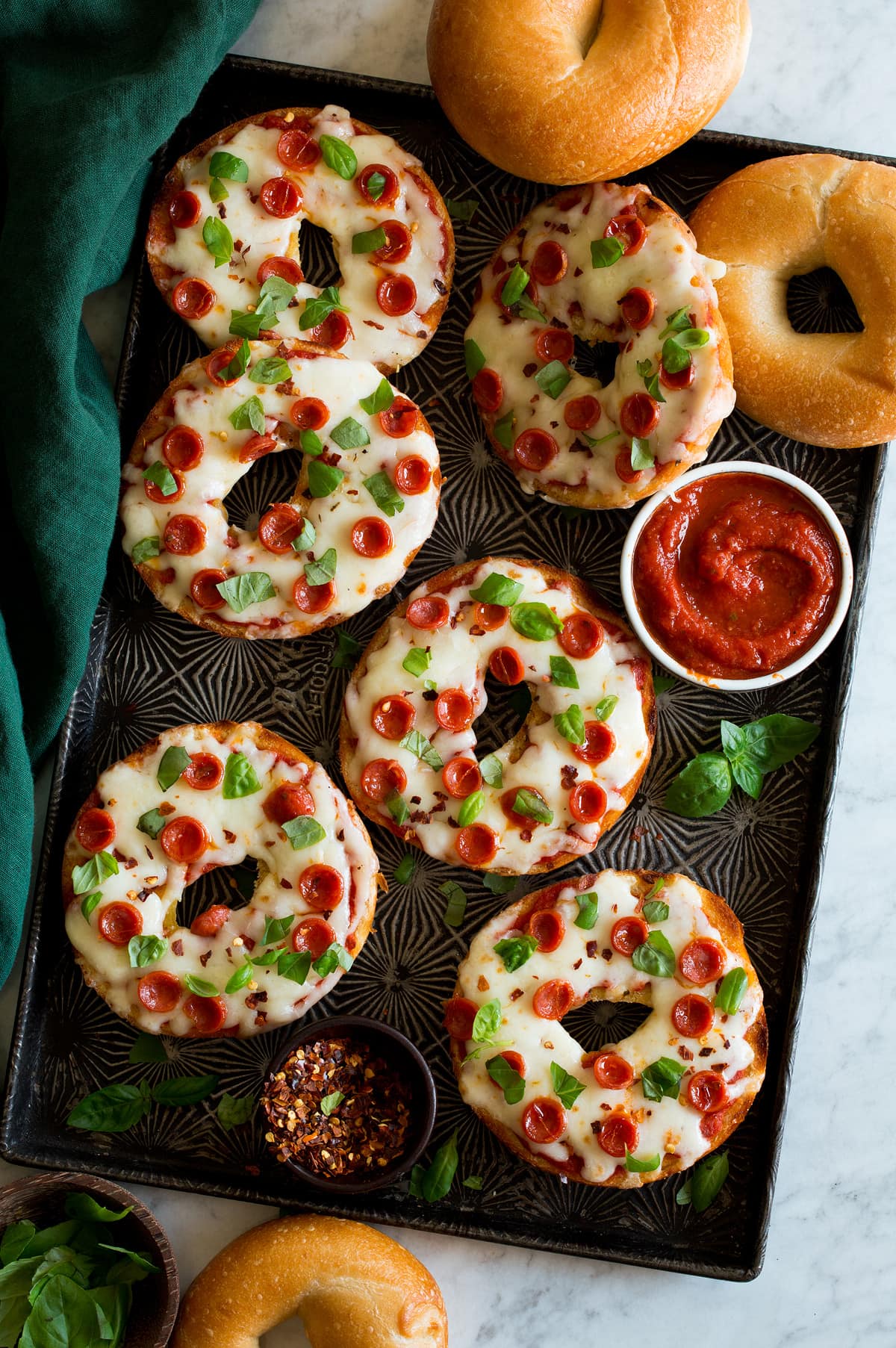 Bagel pizzas on a dark baking sheet.