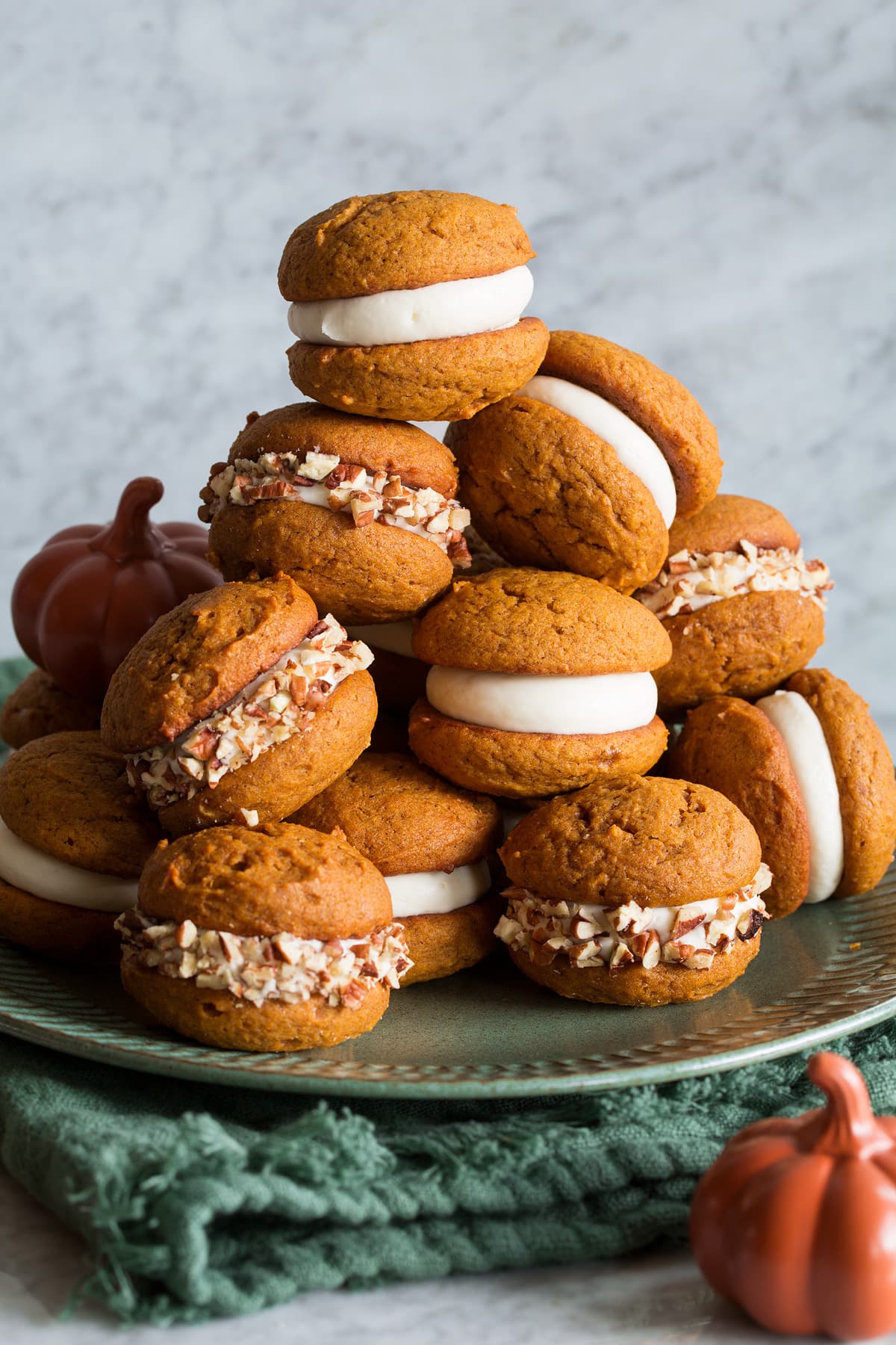 Pumpkin Whoopie Pies Pumpkin Whoopie Pies stacked on a large plate. They are filled with cream cheese frosting and some are covered with chopped pecans.