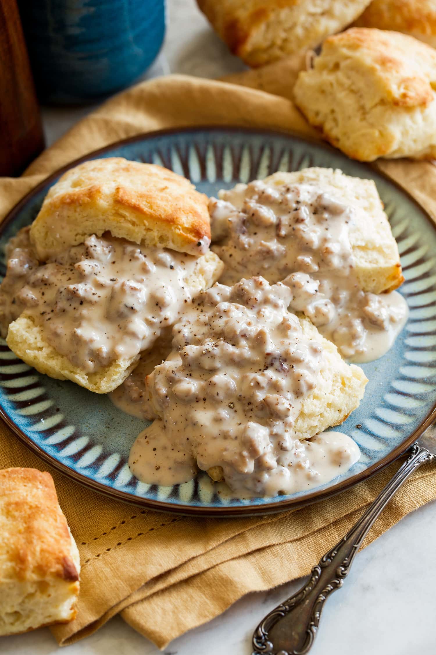 Biscuits and Gravy Three buttermilk biscuits with sausage gravy on a blue plate.