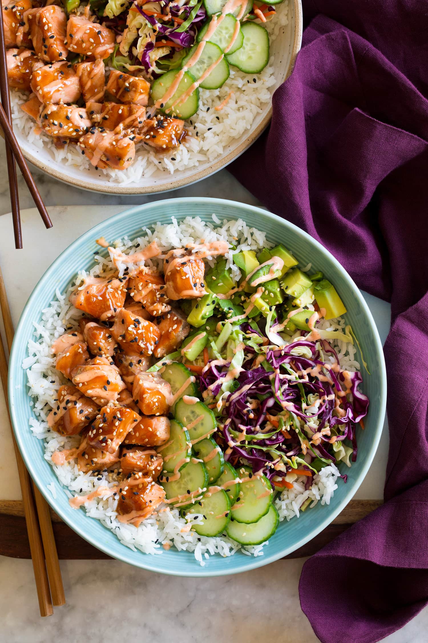Salmon Rice Bowls Layered into a blue bowl is white rice, glazed salmon, cucumber, asian cabbage slaw, avocado, and sesame seeds.