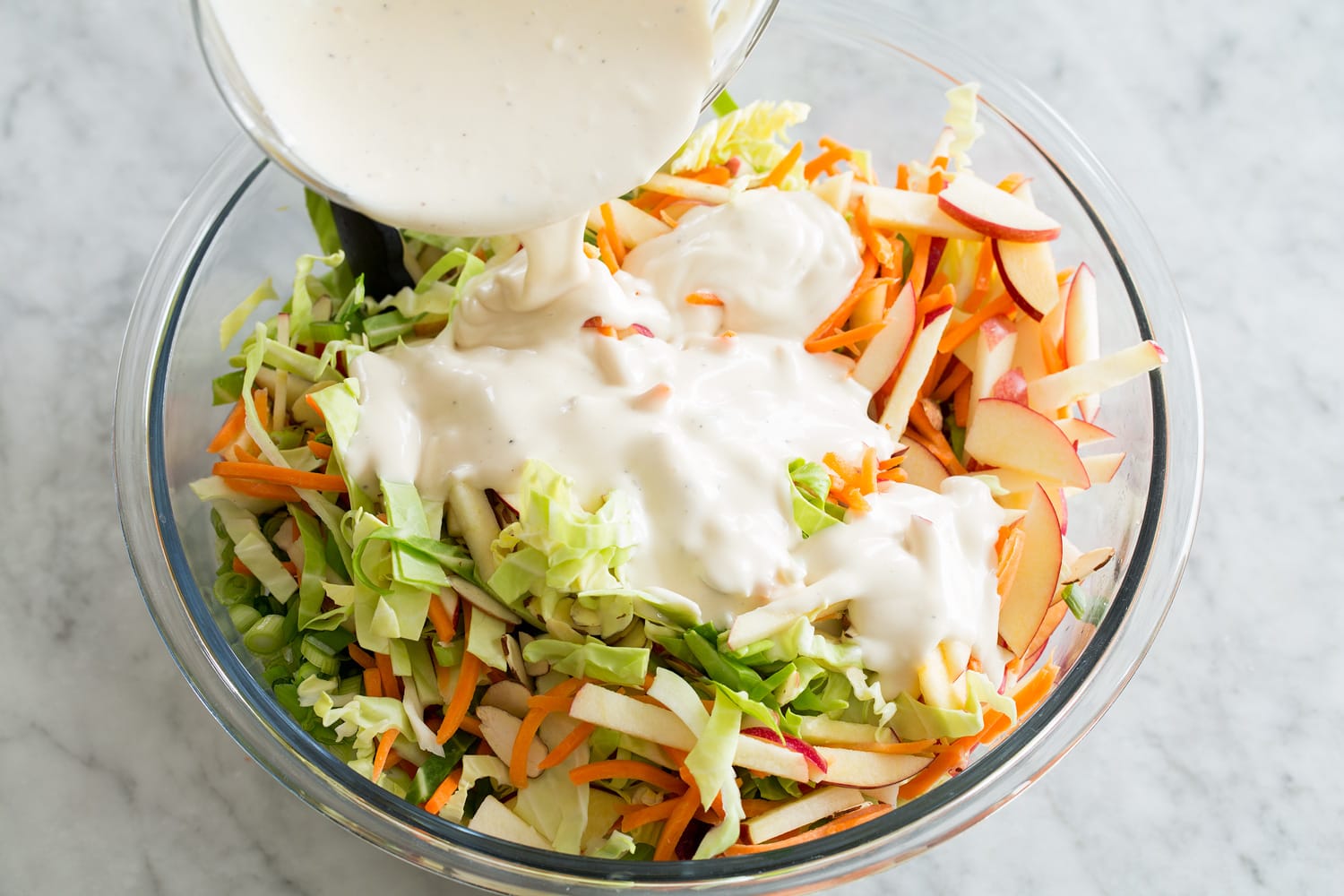 Apple Slaw Slaw being topped with dressing.