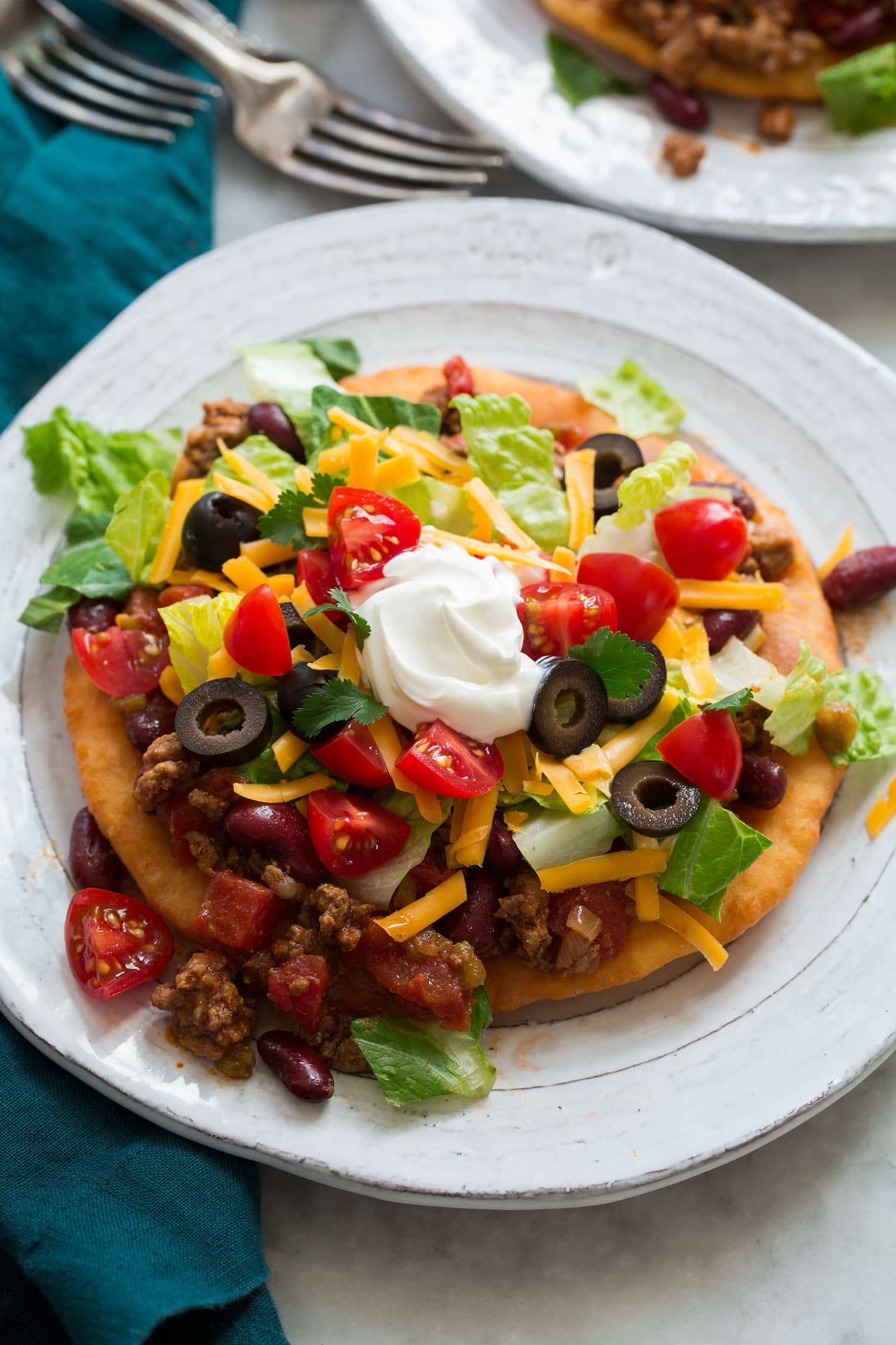 Navajo Tacos Homemade navajo taco on a plate. Made with homemade fry bread, ground beef and bean filling, lettuce, tomatoes, olives and sour cream.