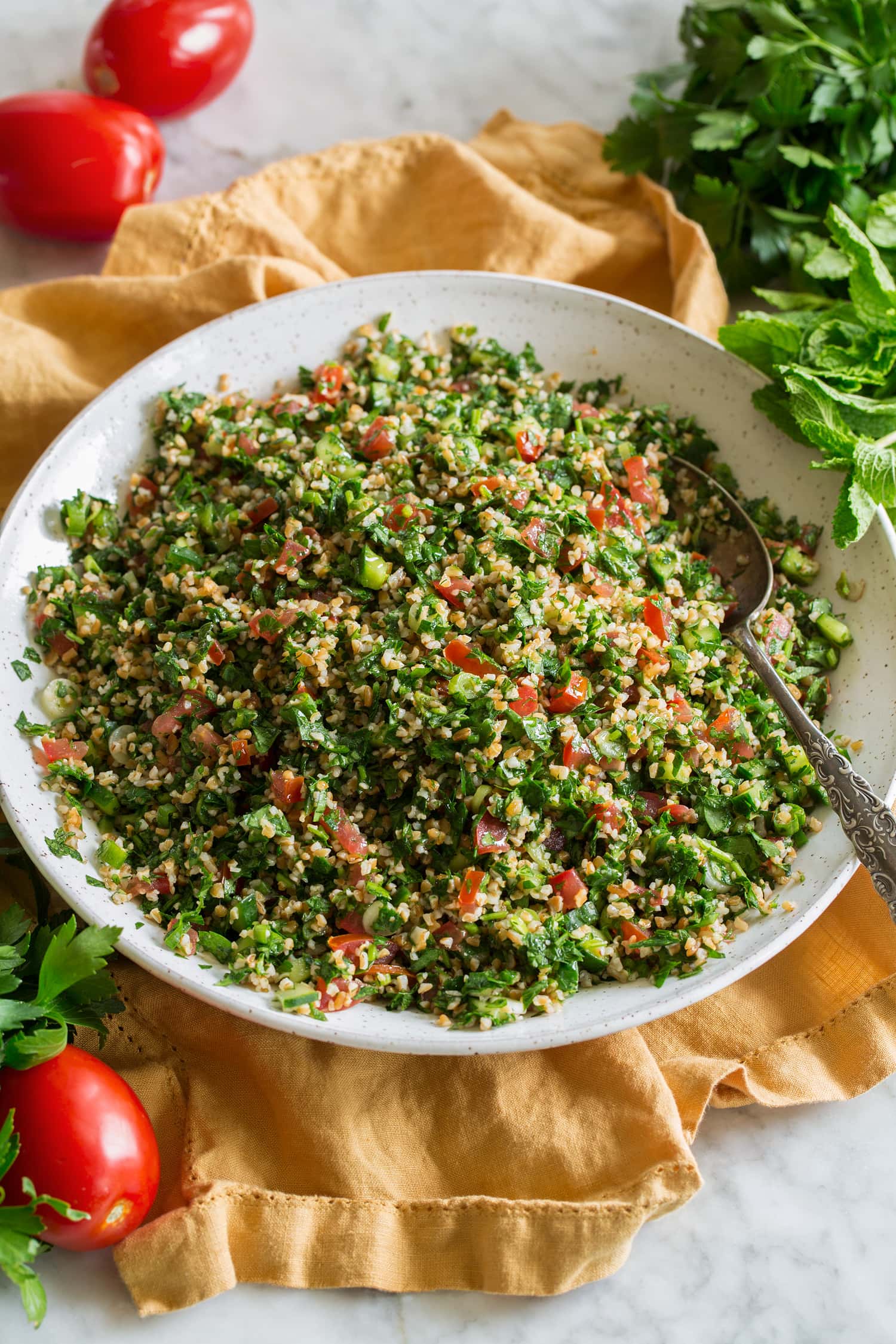 Tabbouleh Herb tabbouleh shown in a white ceramic bowl over a yellow cloth.