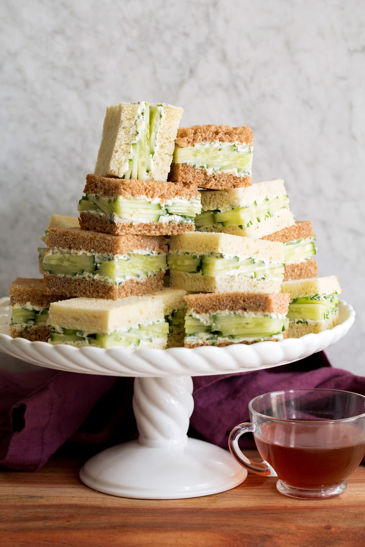 Cucumber Sandwiches Cucumber sandwiches stacked on a white scalloped cake platter.