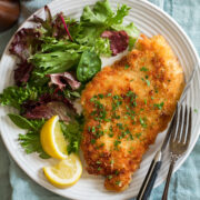 Chicken schnitzel shown served with lemons and a spring salad.