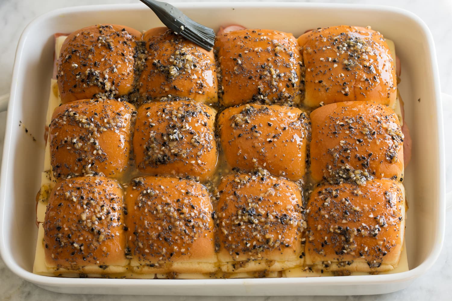 Ham and Cheese Sliders Spreading butter poppy seed mixture over rolls in casserole dish.