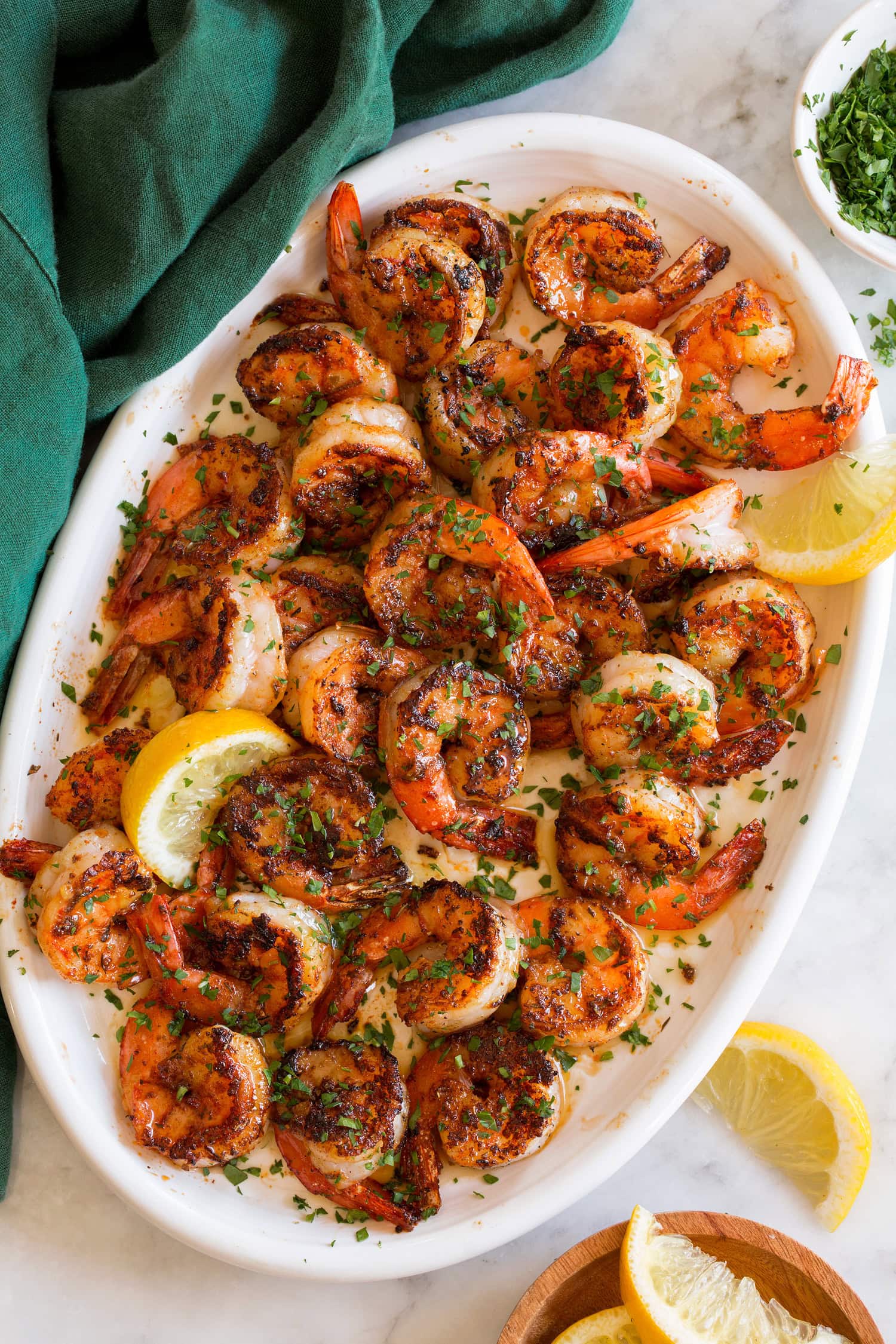 Blackened Shrimp Blackened shrimp garnished with parsley shown on a white oval platter with lemon slices.