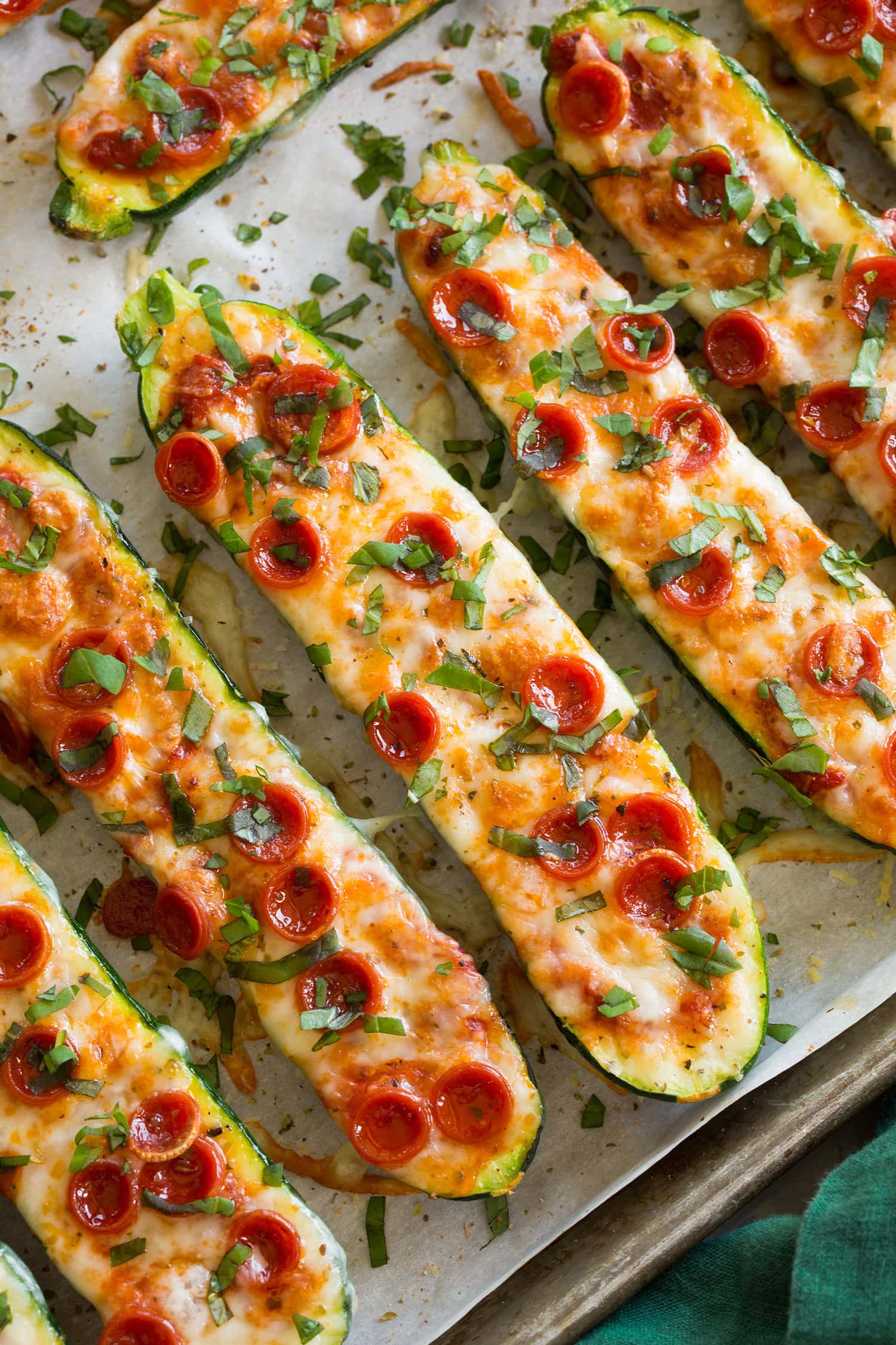 Zucchini Pizza Boats Close up photo of zucchini pizza boats on a parchment lined baking sheet.