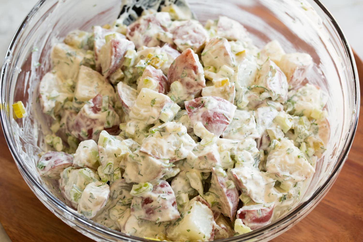 Red Potato Salad Potatoes tossed with potato salad dressing in glass mixing bowl.