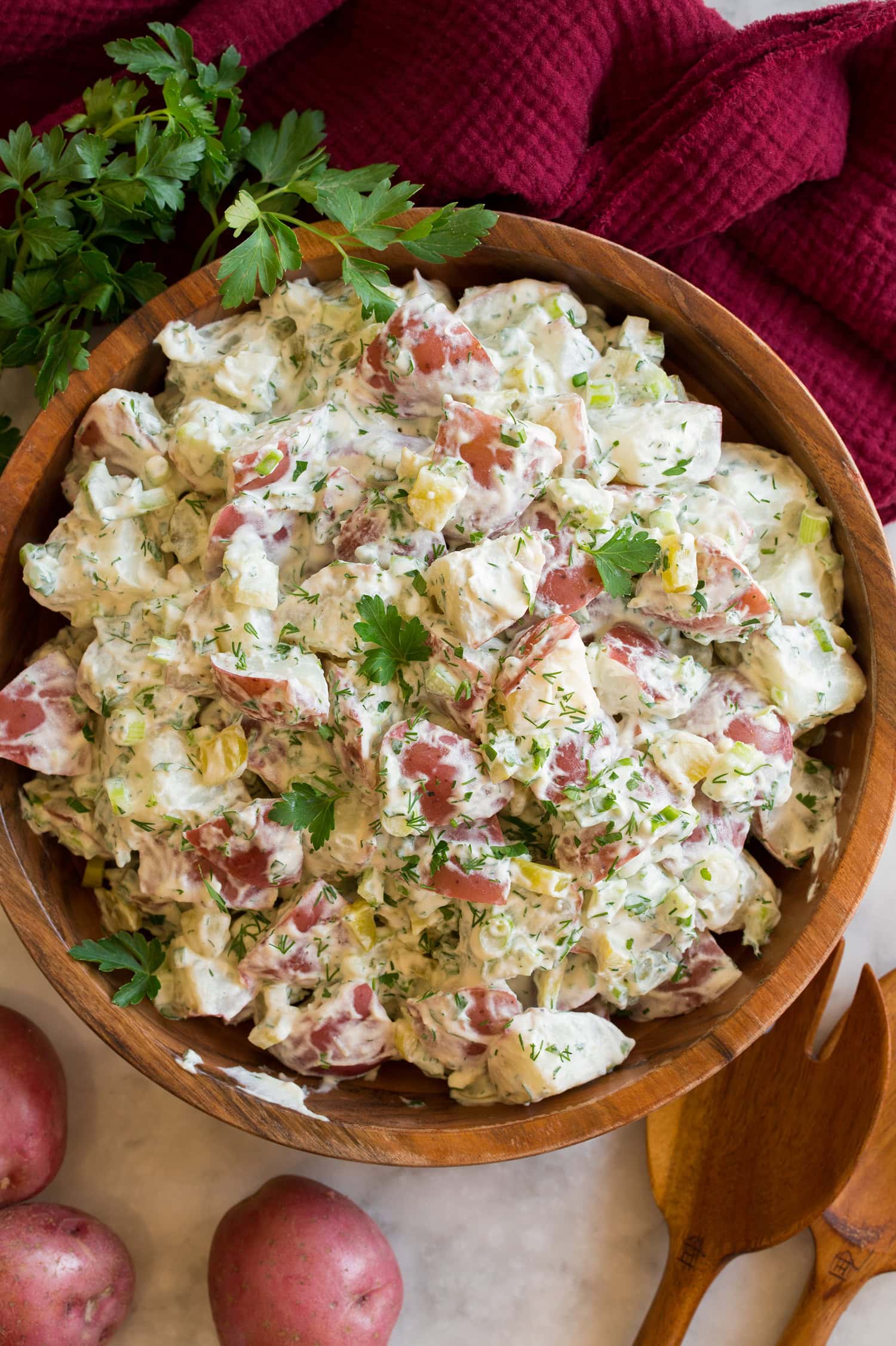 Red Potato Salad Overhead photo of red potato salad in a wooden bowl with a red cloth, whole potatoes, and parsley to the side.