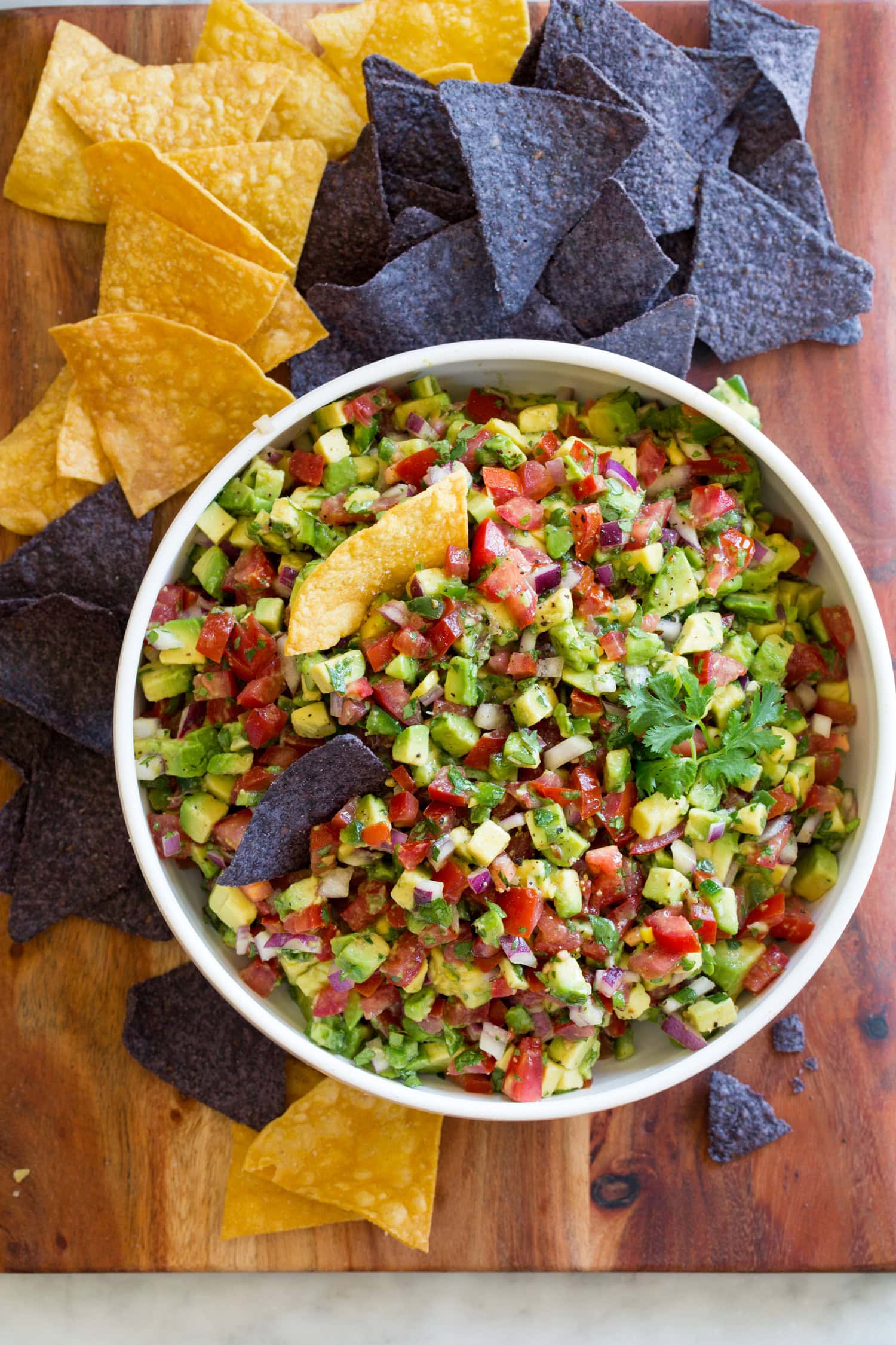 Avocado Salsa Avocado salsa in a bowl with yellow and blue tortilla chips to the side.