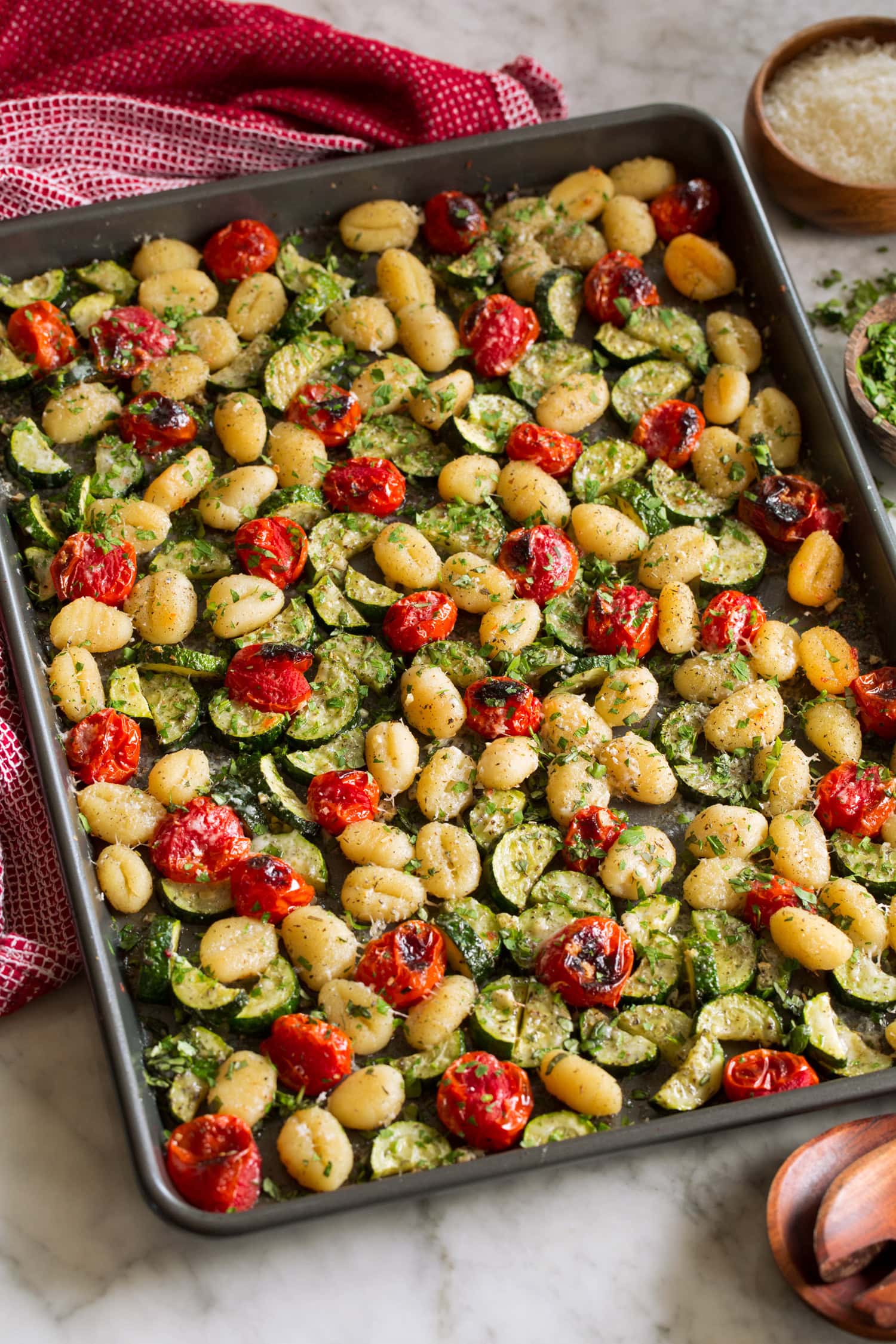 Sheet Pan Gnocchi with Zucchini and Tomatoes Baked gnocchi with vegetables on a dark baking sheet.