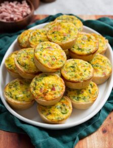Mini quiche stacked on a white oval platter over a teal cloth.