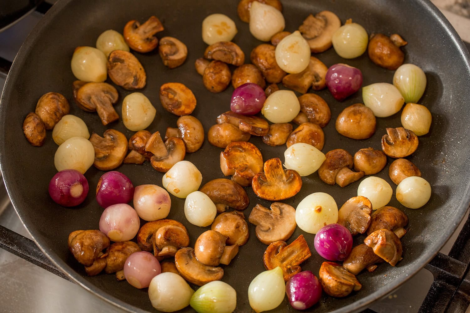 Beef Bourguignon Mushrooms and pearl onions being sauteed in a skillet.