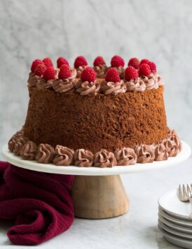 Whole chocolate angel food cake on a white marble and wood cake stand.