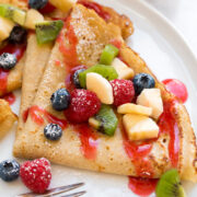 Close up photo of healthy oat crepes with chopped fruit and berry syrup.