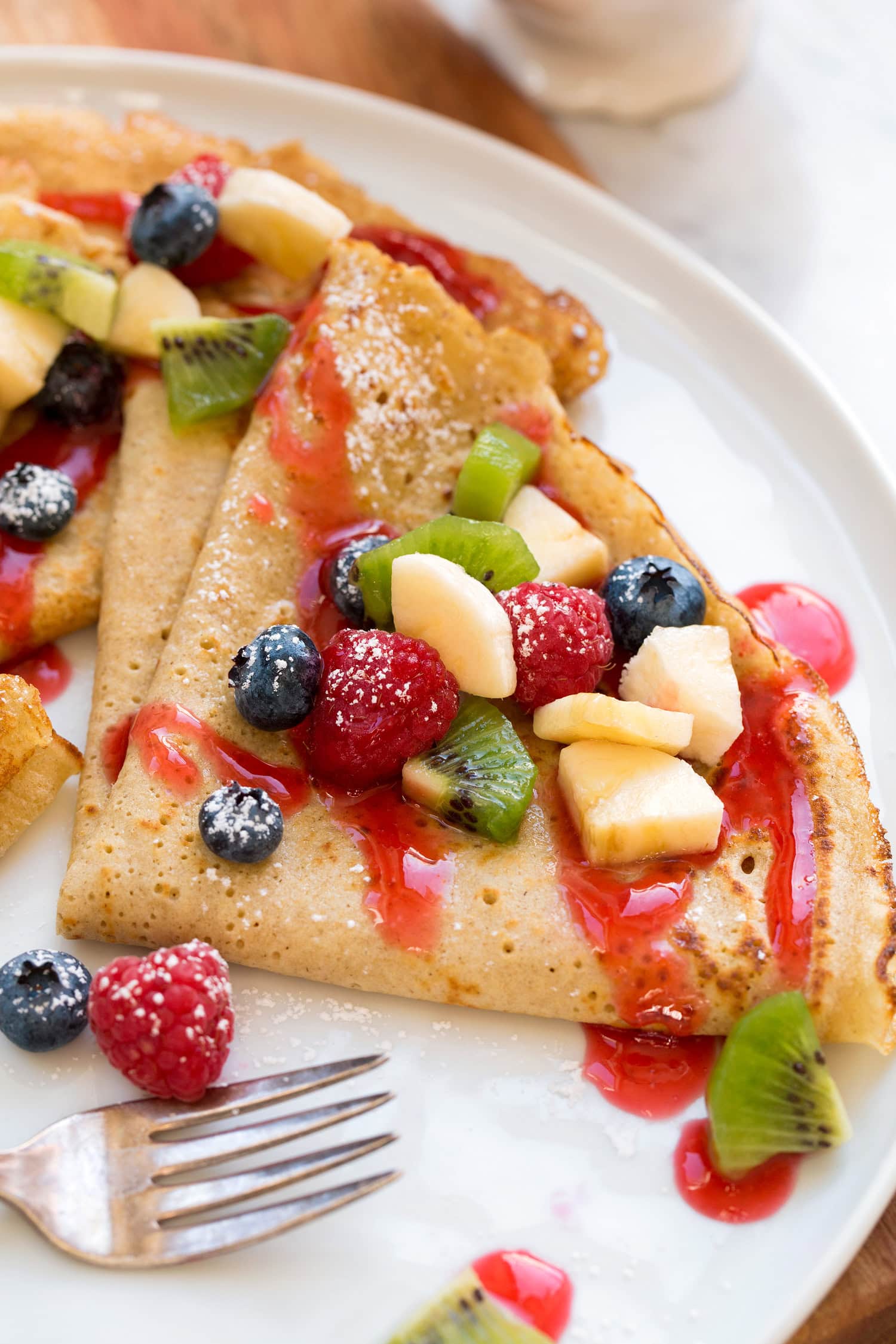 Close up photo of healthy oat crepes with chopped fruit and berry syrup.