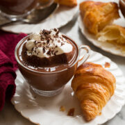French hot chocolate in a small glass mug served with a croissant on the side.