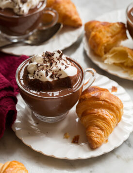 French hot chocolate in a small glass mug served with a croissant on the side.