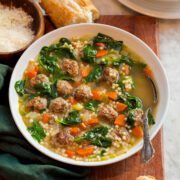 Italian wedding soup in a serving bowl with baguette bread and parmesan shown for serving.