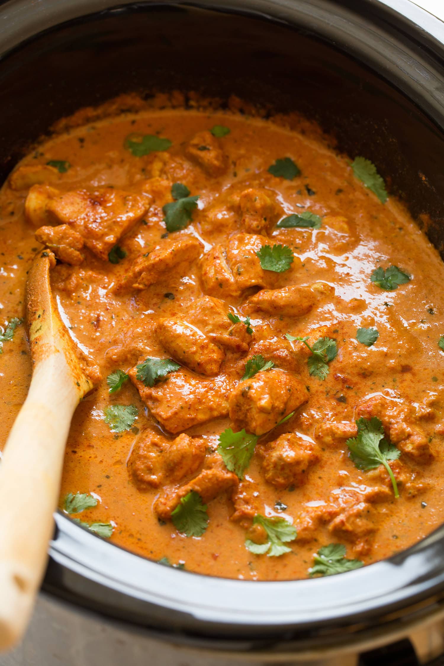 Slow cooker chicken tikka masala garnished with cilantro in a black crockpot.