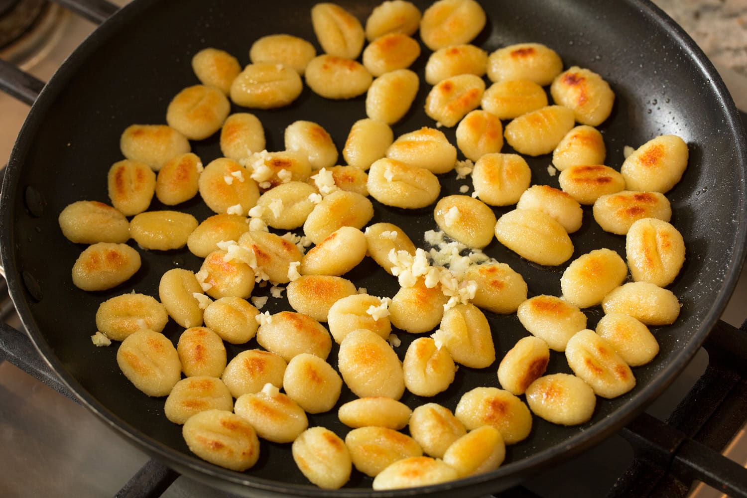 Pan Fried Gnocchi Garlic added to browned sauteed gnocchi in skillet.