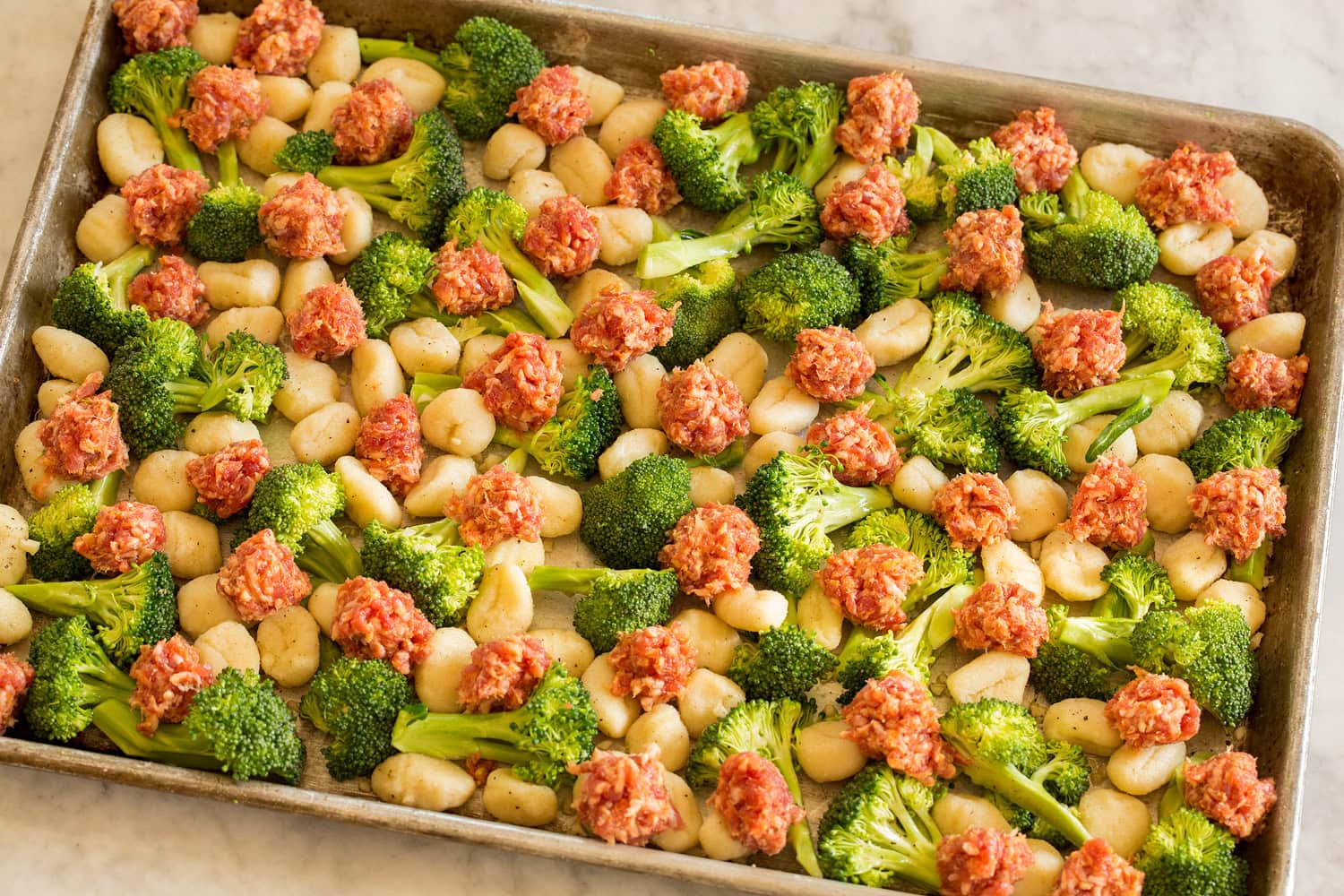 Sheet Pan Gnocchi with Sausage and Broccoli Raw sausage crumbles layered over broccoli and gnocchi tossed together on a sheet pan.